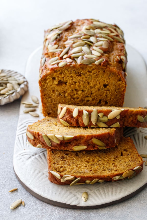 Sliced Spiced Pumpkin Banana Bread on a ceramic plate, dish of pepitas on the side.