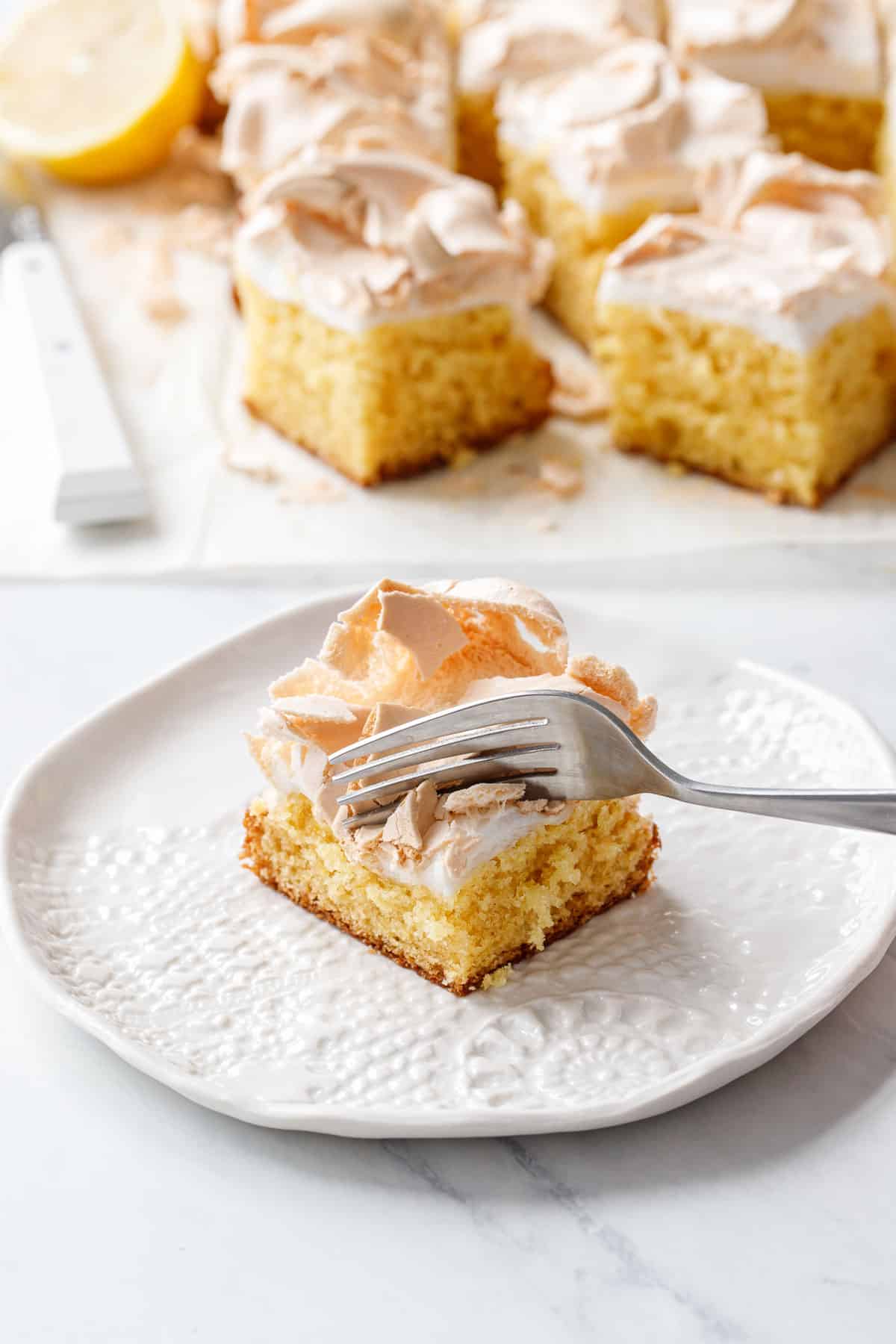 Fork cutting into a square of Lemon Meringue Butter Cake, shattering the toasted meringue topping as it goes.