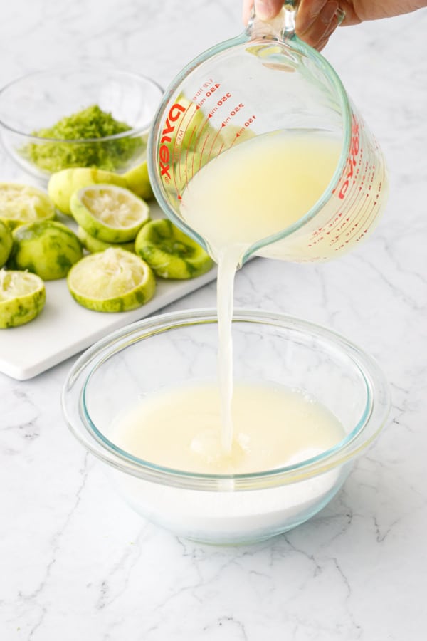 Pouring fresh squeezed lime juice into a bowl with white sugar.