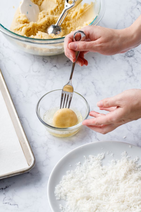 Dipping the flattened dough ball into a bowl with egg whites.