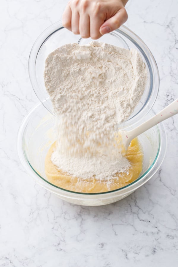 Pouring dry ingredients from one bowl into mixing bowl with other mixed ingredients.