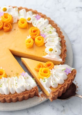 Mango Lime Tart with a slice cut out of it to show the creamy texture inside, decorated with whipped cream and edible flowers.