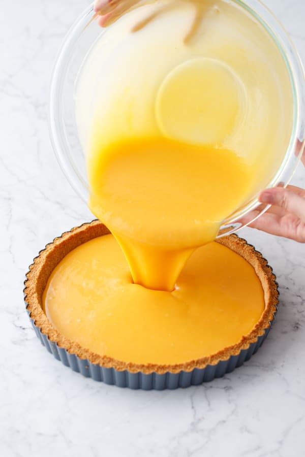 Pouring the Mango Lime Tart filling into graham cracker crust until nearly full.