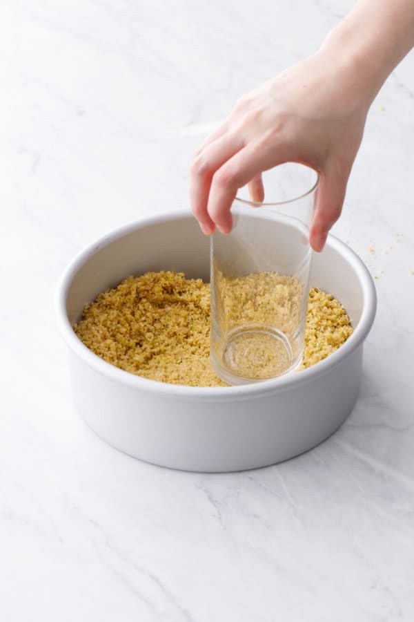 Pressing the crust mixture into the cheesecake pan using a tall glass.