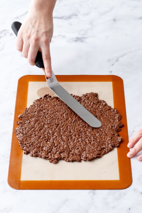 Spreading the croustillant into a thin even layer on a silicone mat using a large offset metal spatula.