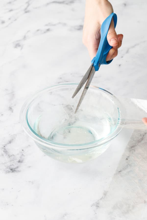 Cutting strips of leaf gelatin over a bowl of water to soften.