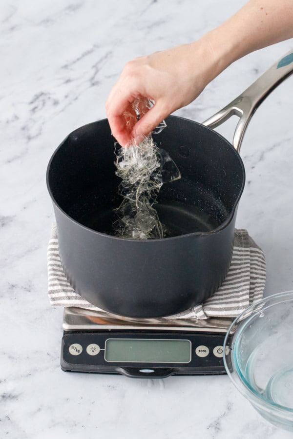 Adding the softened leaf gelatin to the saucepan with the hot sugar syrup.