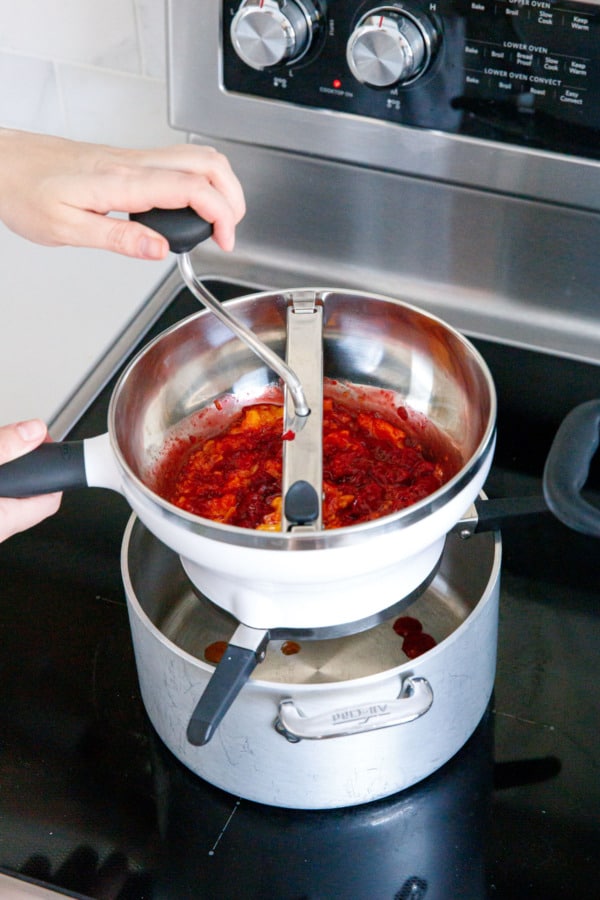 Running fresh mangoes and raspberries through a food mill to remove seeds and fibrous bits.