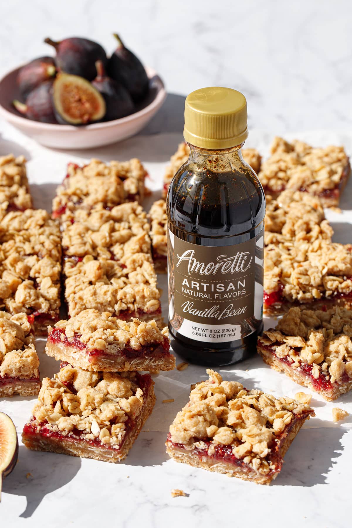 Bottle of Amoretti Vanilla Bean flavoring sitting amidst messy cut squares of Fig, Apple & Vanilla Crumb Bars.