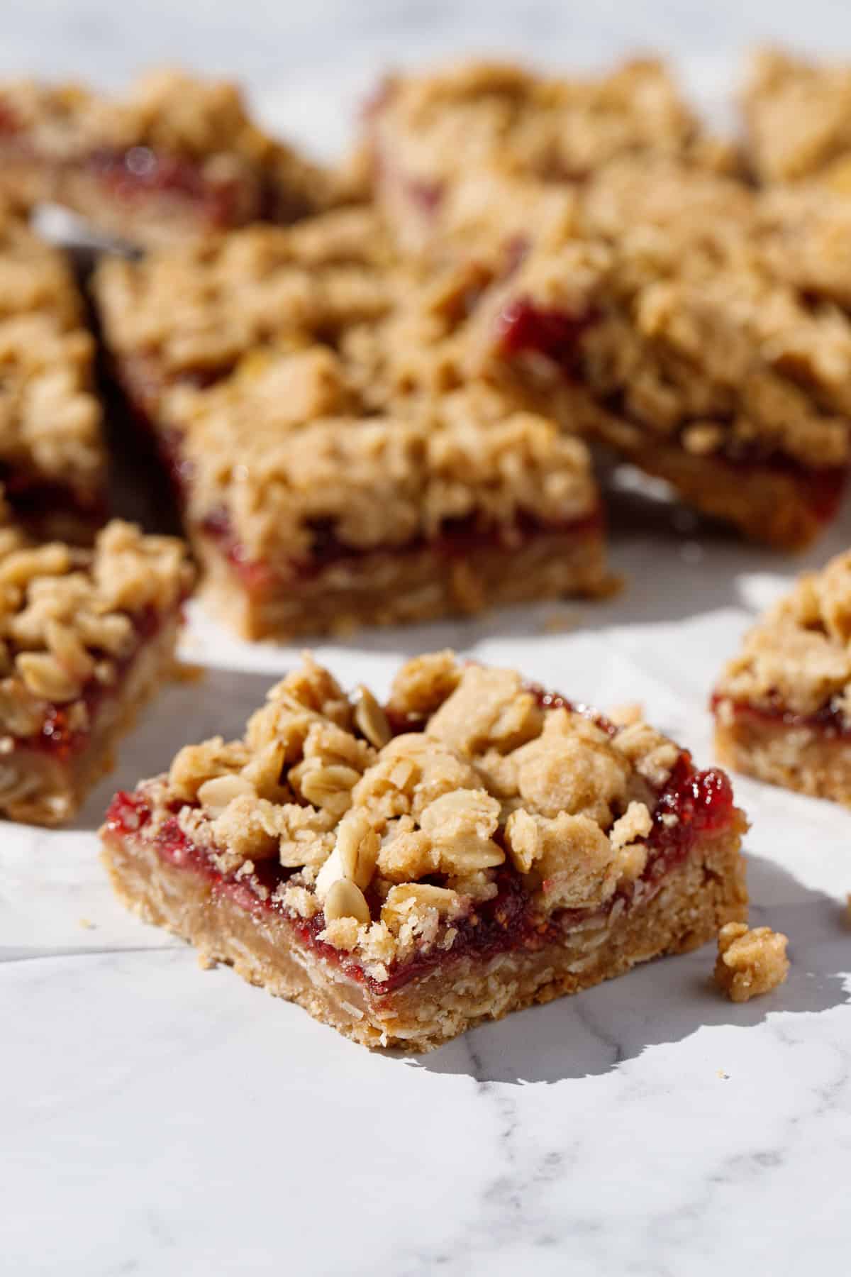 Closeup, one square Fig, Apple & Vanilla Crumb Bar in the foreground showing the purple layer of fig apple jam and messy oat crumble on top.
