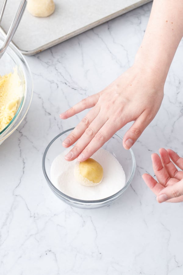 Rolling the shaped ball of cookie dough in a bowl of granulated sugar until coated.