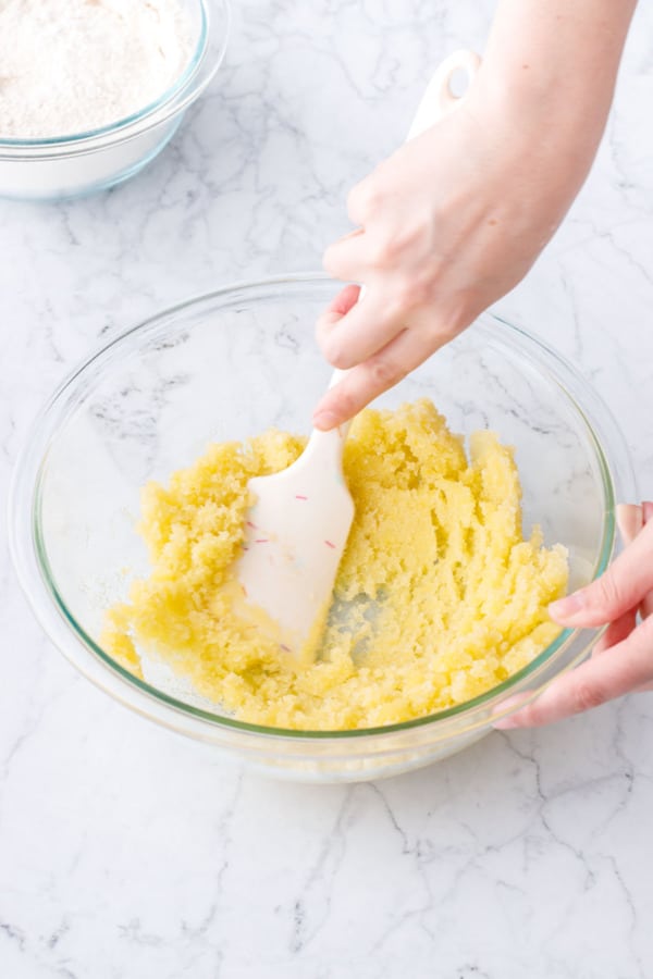 Spatula mixing the sugar and olive oil dough, showing the pasty, wet-sand-like texture.