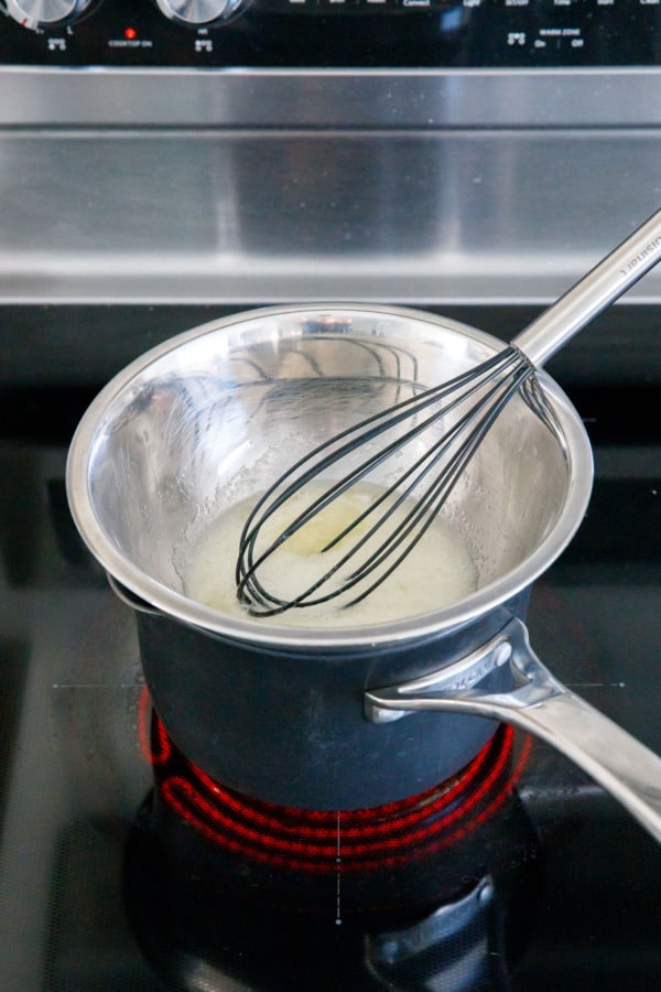 Stainless bowl on top of a saucepan with liquid egg whites and sugar and whisk.