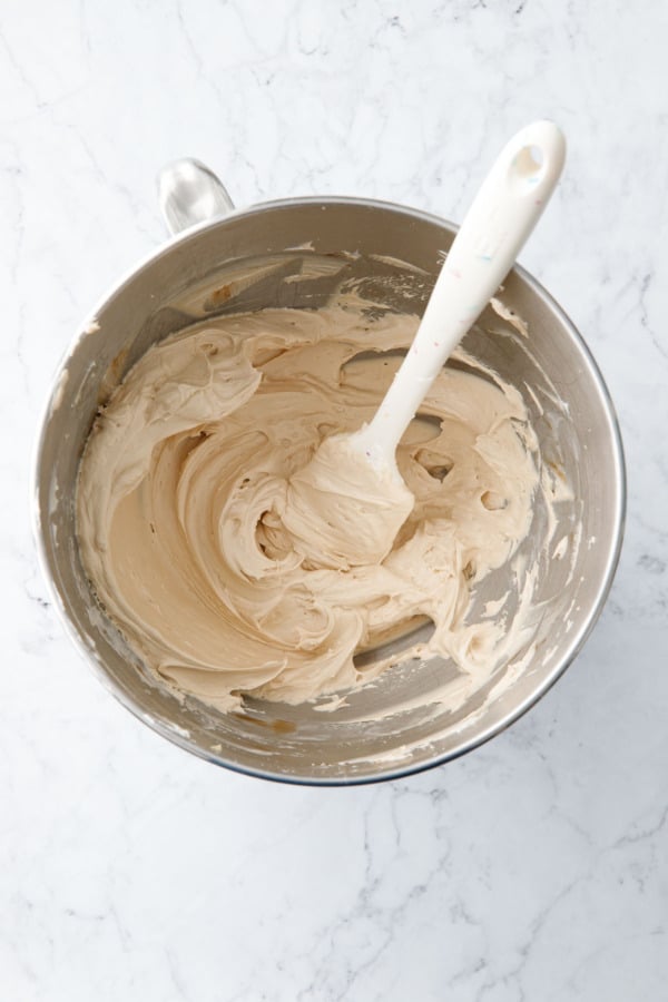 Top down view of mixing bowl with Salted Caramel Meringue Buttercream and a white rubber spatula in the bowl.