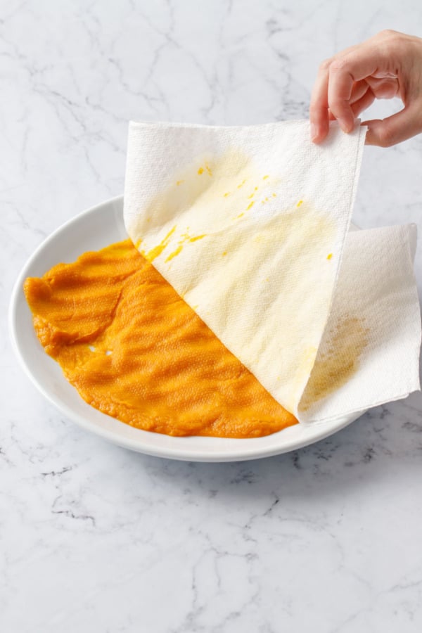 Peeling off saturated paper towels from the pumpkin puree on a plate.