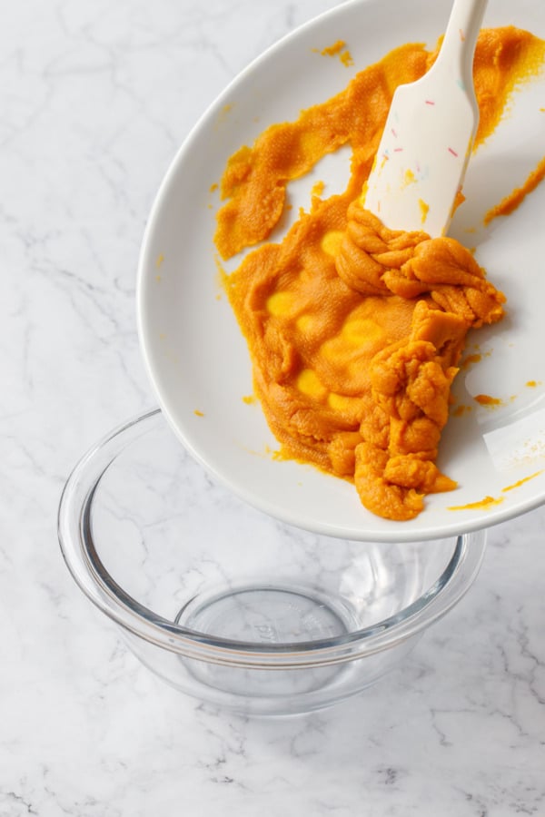Scraping drained pumpkin puree into a bowl.