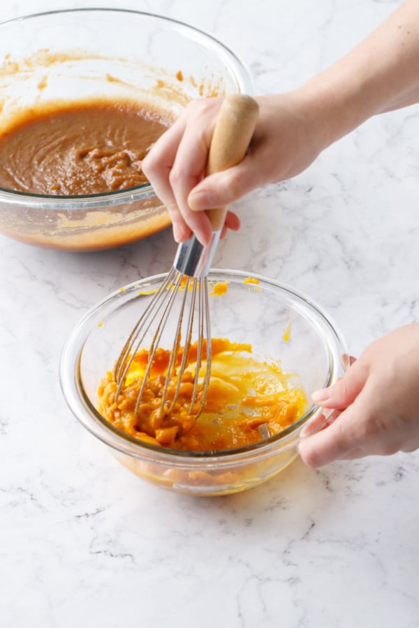 Whisking pumpkin puree and egg yolks in a small glass mixing bowl, another bowl of batter in the background.