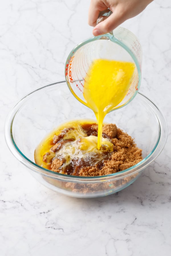 Pouring melted butter from a glass measuring cup in to a mixing bowl with dark brown sugar.