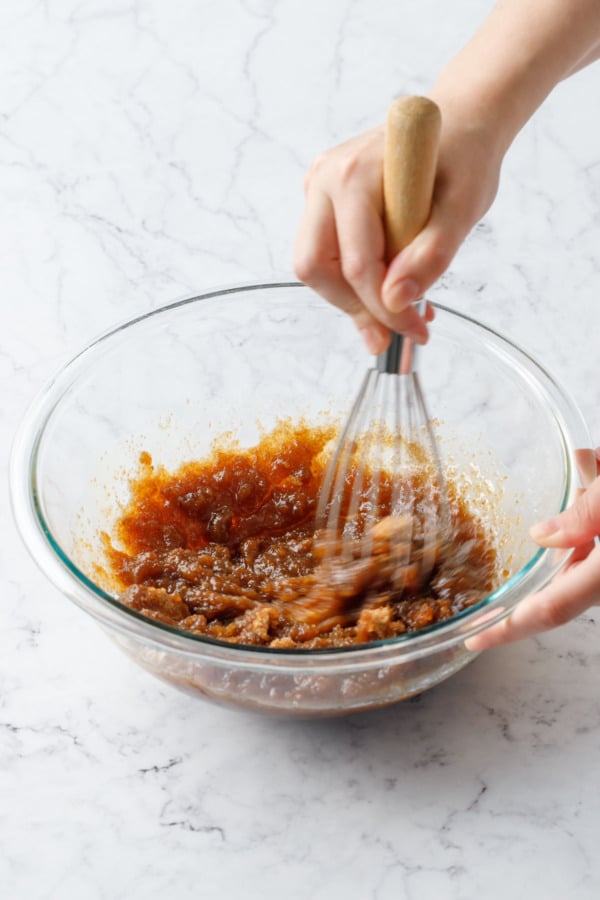 Whisking brown sugar with melted butter in a glass mixing bowl; mixture appears greasy and separated.