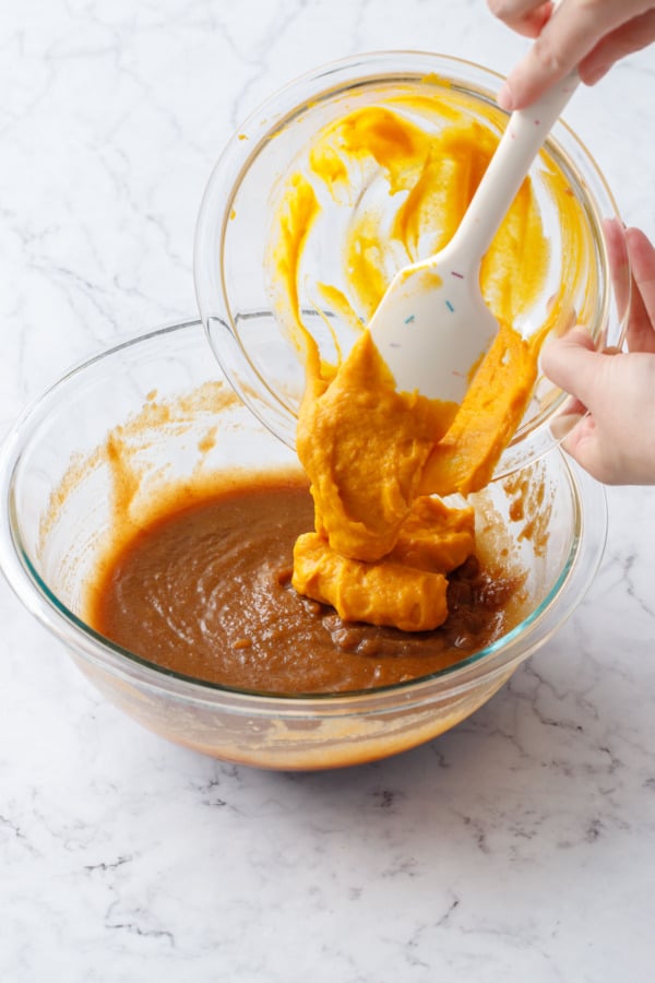 Pouring orange pumpkin mixture into another mixing bowl with brown sugar and butter mixture.