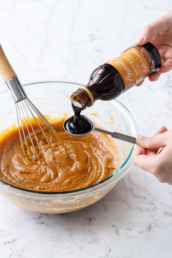 Measuring out Amoretti Natural Salted Caramel Artisan Flavor Paste over bowl with pumpkin cookie dough batter and a whisk sitting in the bowl.