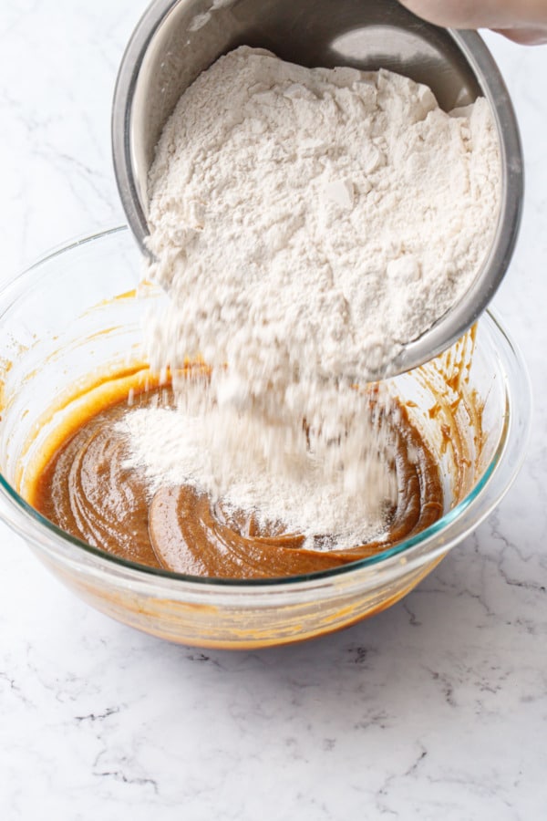 Pouring a bowl of flour and other dry ingredients into another bowl with wet ingredients.