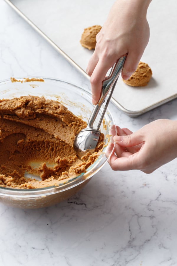 Large cookie scoop scooping dough out of mixing bowl.