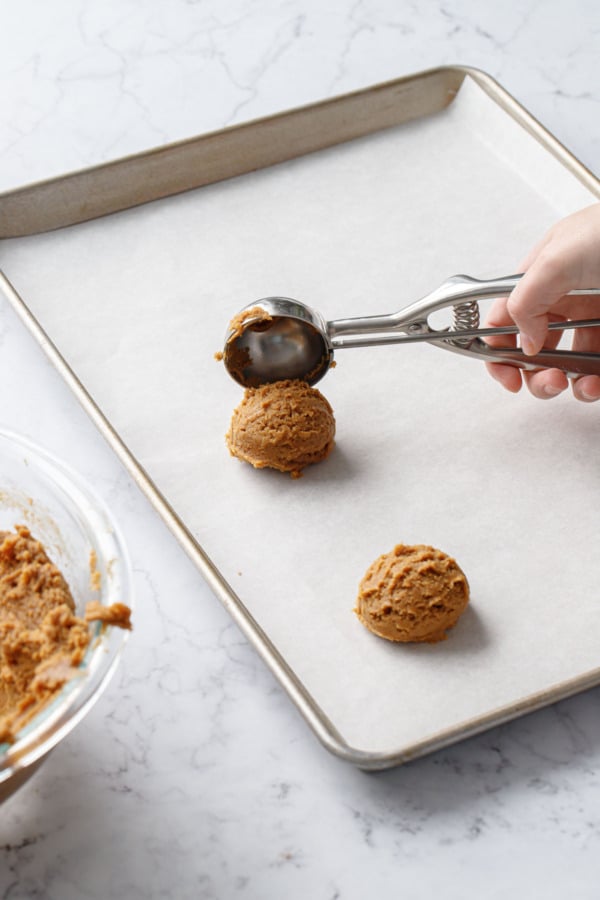 Dropping a scoop of cookie dough from the cookie scoop onto a parchment-lined cookie sheet.