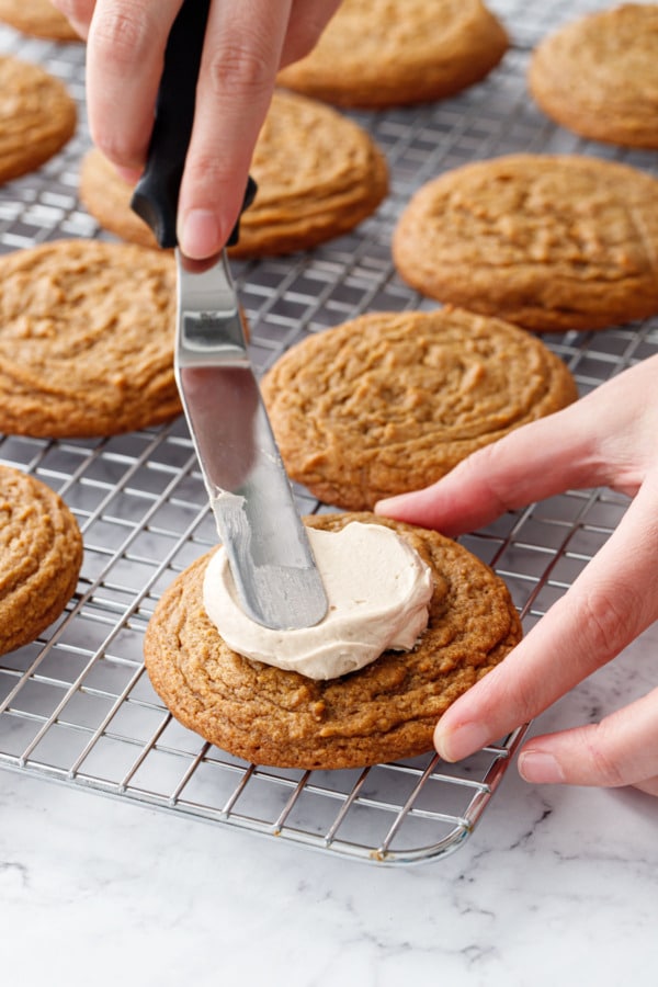 Offset spatula spreading caramel buttercream on top of pumpkin cookie.
