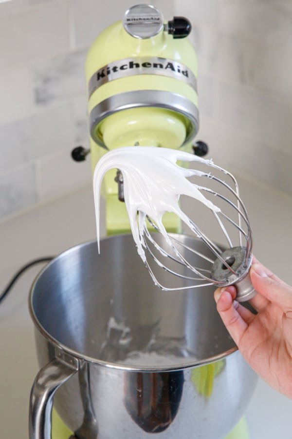 Electric mixer whisk showing the meringue when it is smooth and glossy and forming a medium peak on the end of the whisk.