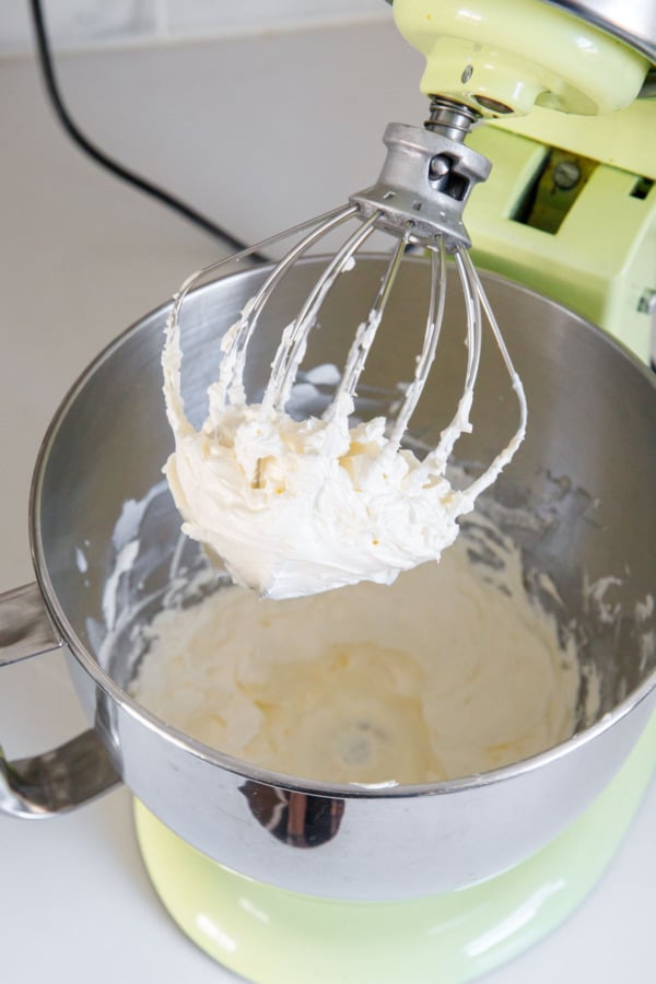 Stand mixer with whisk attachment showing consistency of frosting after adding all of the butter.
