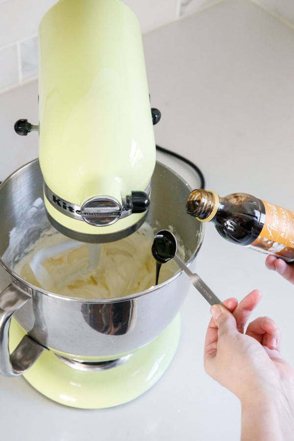Measuring caramel flavoring and pouring it into the stand mixer bowl with fluffy frosting.
