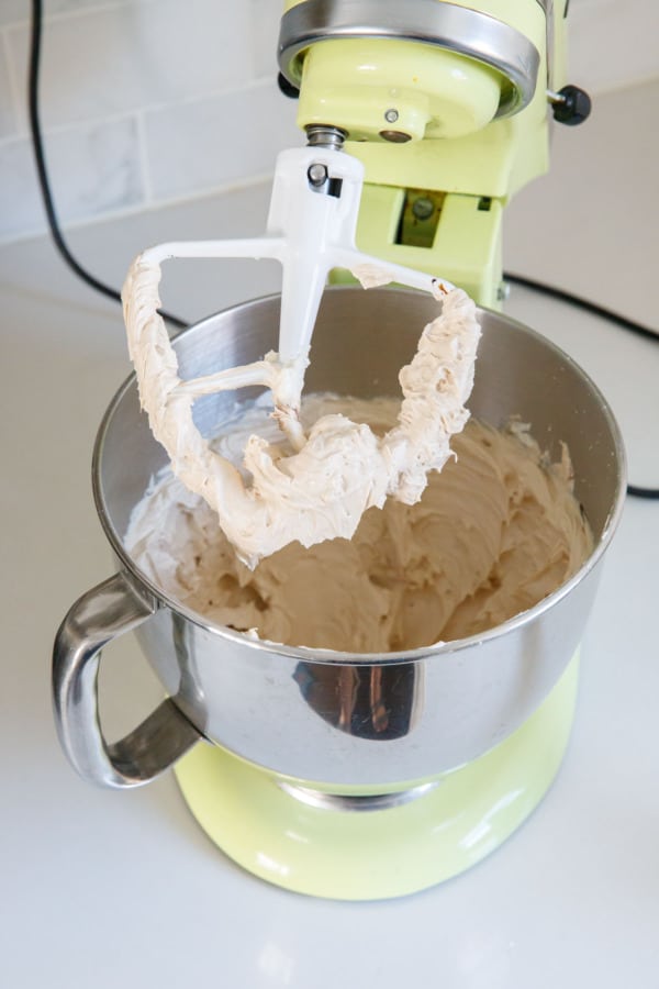 Paddle attachment lifted out of a stand mixer, showing the smooth and fluffy consistency of the final caramel frosting.