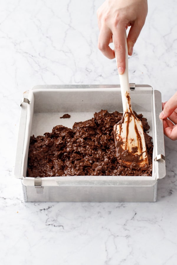 Silicone spatula spreading feuilletine mixture into an even layer in baking pan.