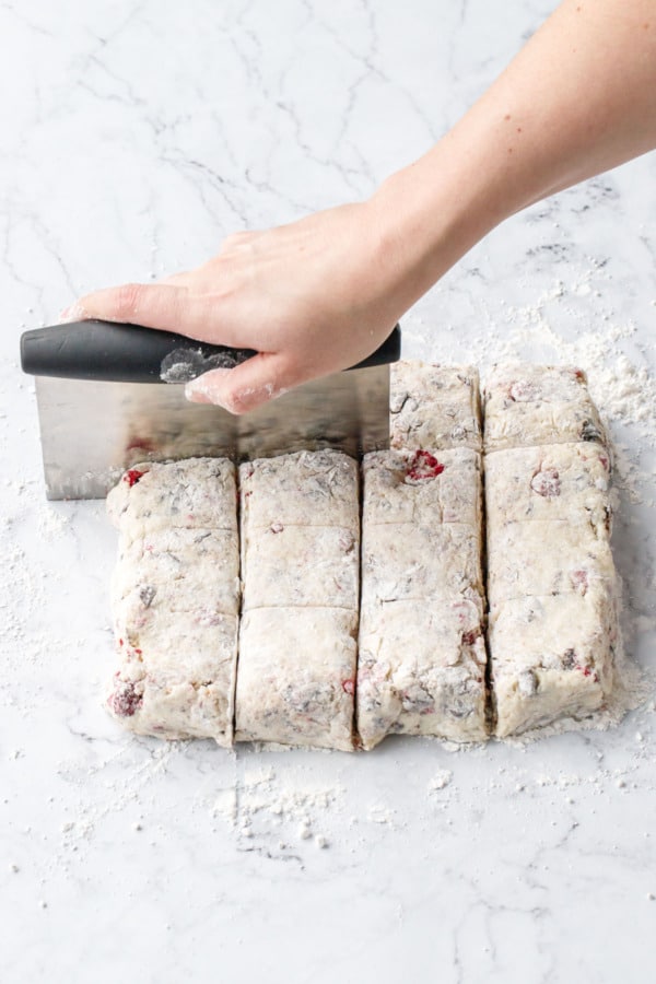 Bench scraper cutting square of scone dough into individual square scones.