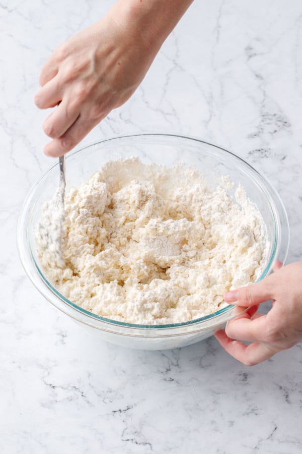 Using a fork to mix together the shaggy textured dough in a glass mixing bowl.