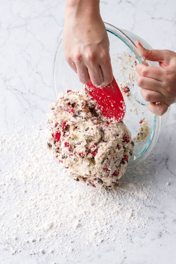 Pastry scraper scraping dough out of mixing bowl and onto a floured marble surface.
