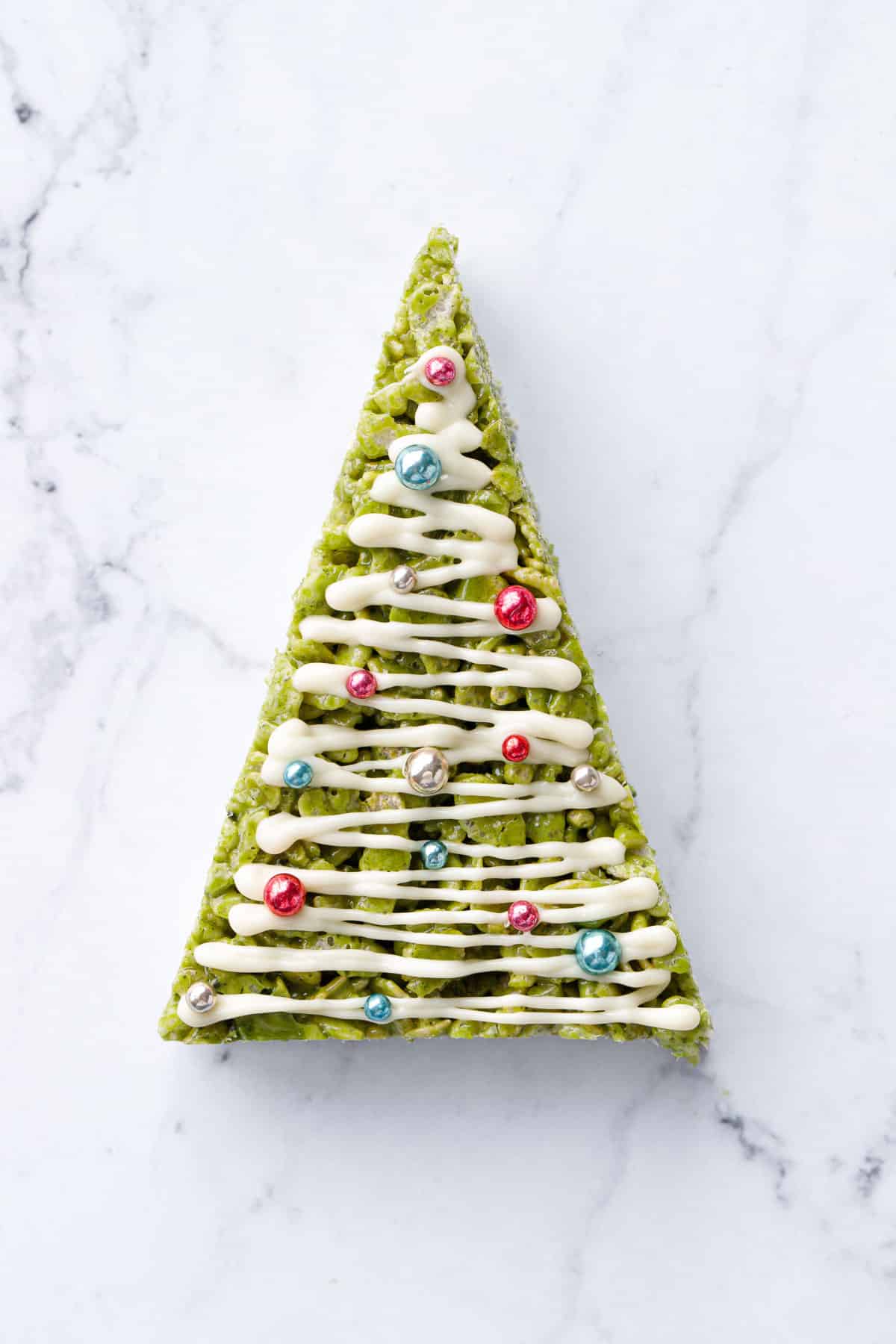 Single Matcha Rice Crispy Treat cut into a sharp triangle and decorated like a Christmas tree with a drizzle of white chocolate and metallic sprinkle "ornaments".