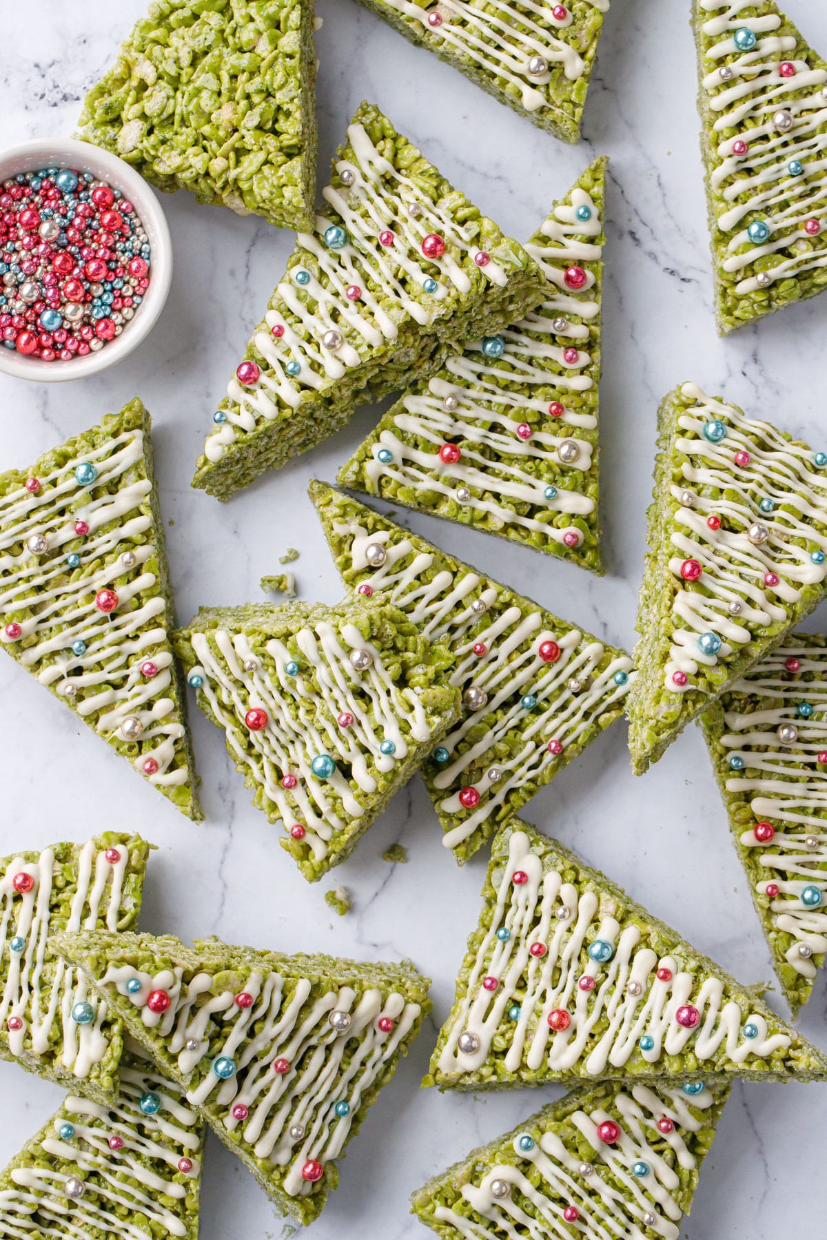 Overhead, randomly arranged Matcha Rice Crispy Treats on a marble background with a bowl of metallic sprinkles.