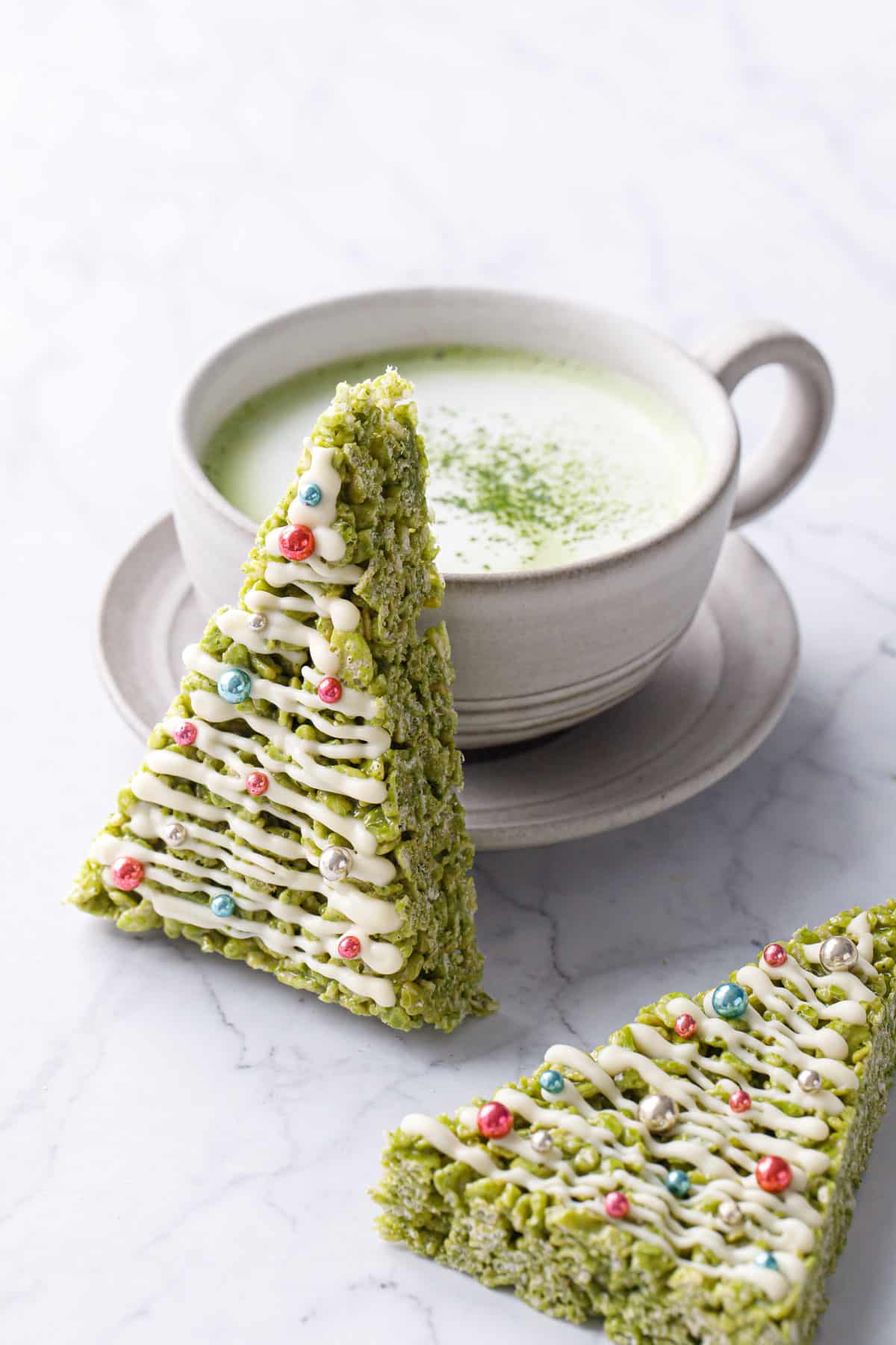 Matcha Rice Crispy Treats cut into a triangle and decorated like a Christmas tree, leaning up against a matcha latte.