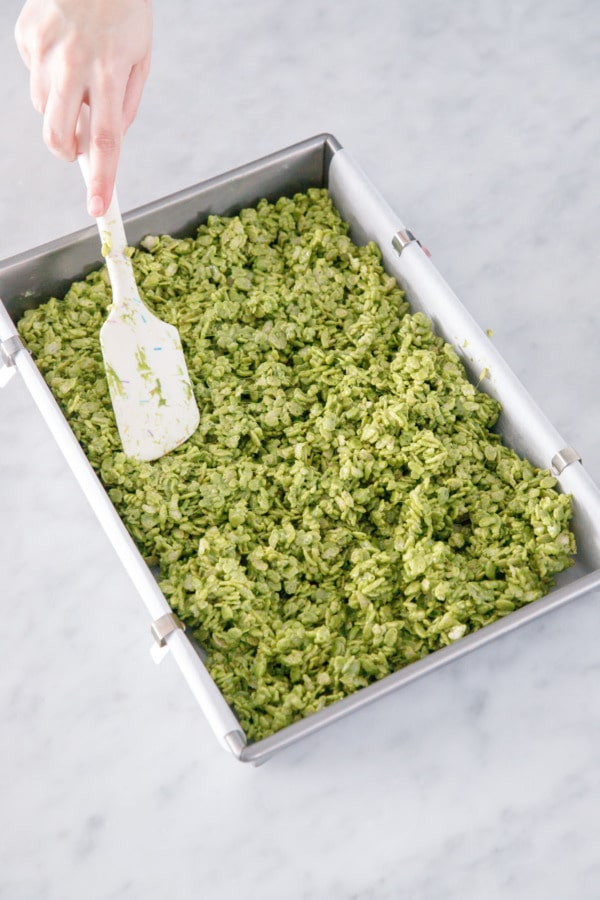Gently pressing marshmallow cereal mixture into baking pan with a rubber spatula.