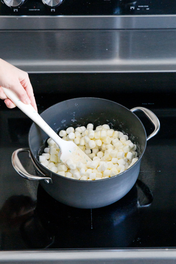 Spatula stirring mini marshmallows in a saucepan on the stovetop.