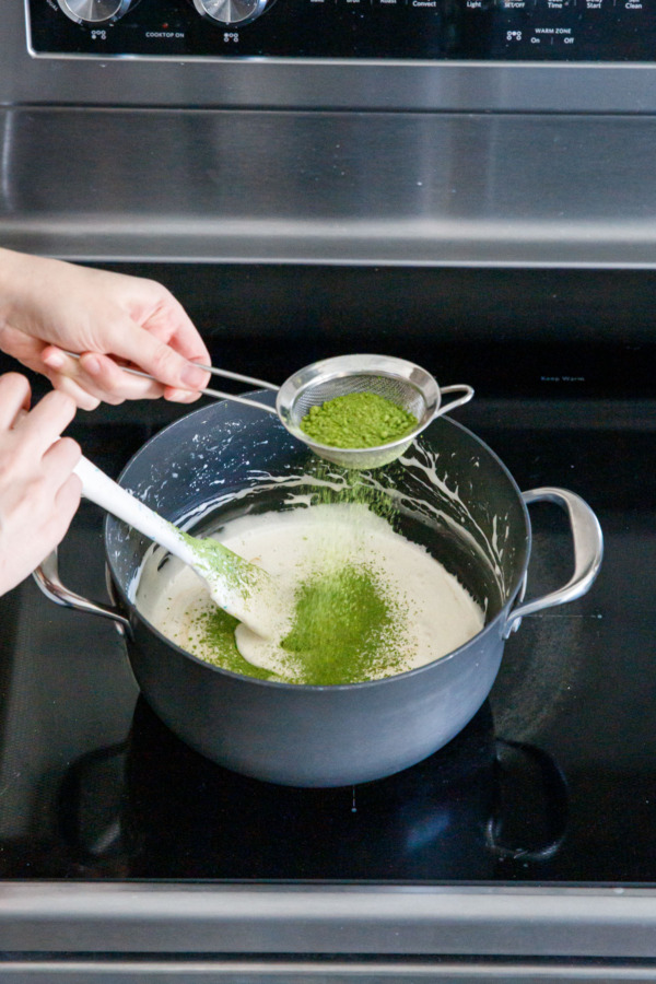 Sifting matcha green tea powder into saucepan with melted marshmallow mixture.