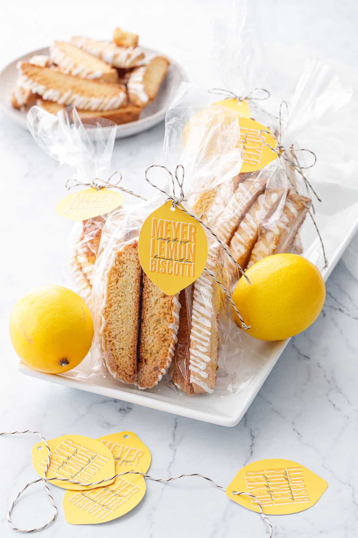 White plate with Meyer Lemon Biscotti in clear cello gift bags, tied with twine and a lemon-shaped gift tag.