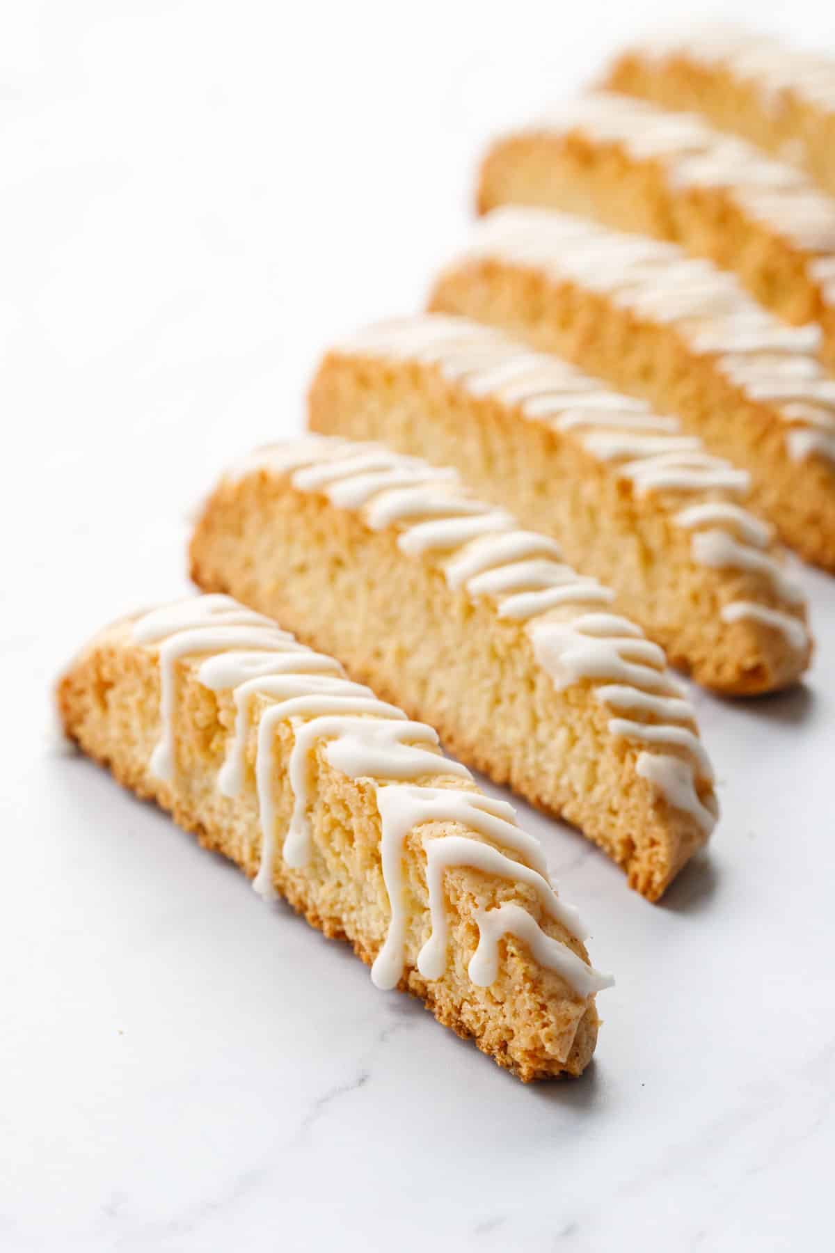 Row of Meyer Lemon Biscotti, drizzled with white chocolate lemon glaze, cookies standing on their sides with a shallow depth of field.
