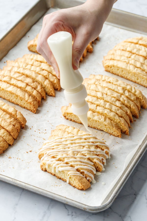 Drizzling bunches of twice-baked biscotti cookies with a white chocolate and lemon glaze in a squeeze bottle.
