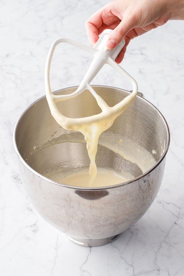Mixer paddle lifting out of the mixing bowl, showing the light color and ribbon-like texture of the eggs after beating with the sugar.