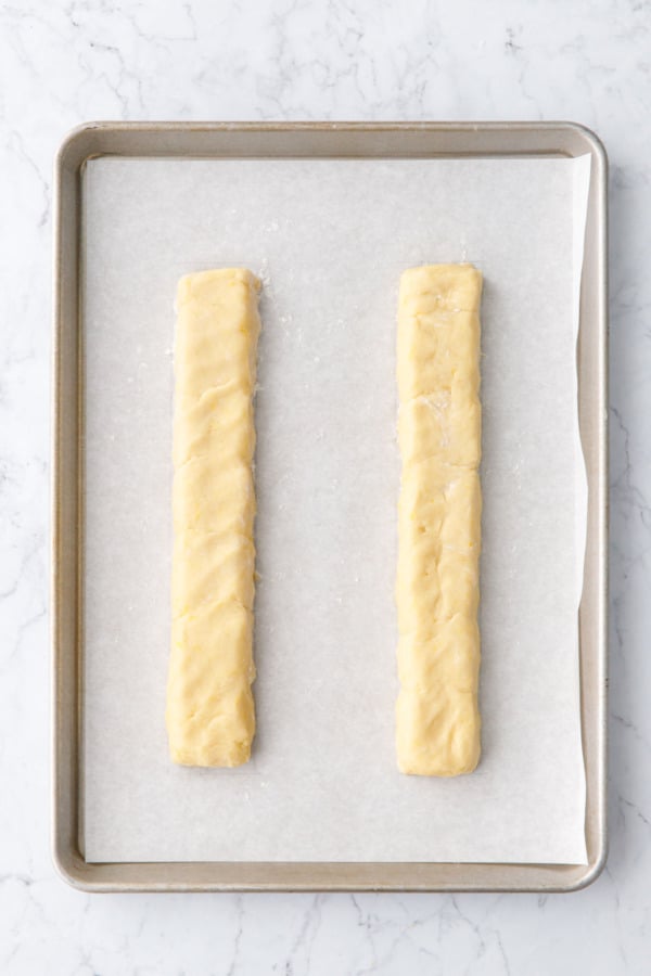Overhead, two logs of biscotti cookie dough on a parchment-lined cookie sheet before baking.