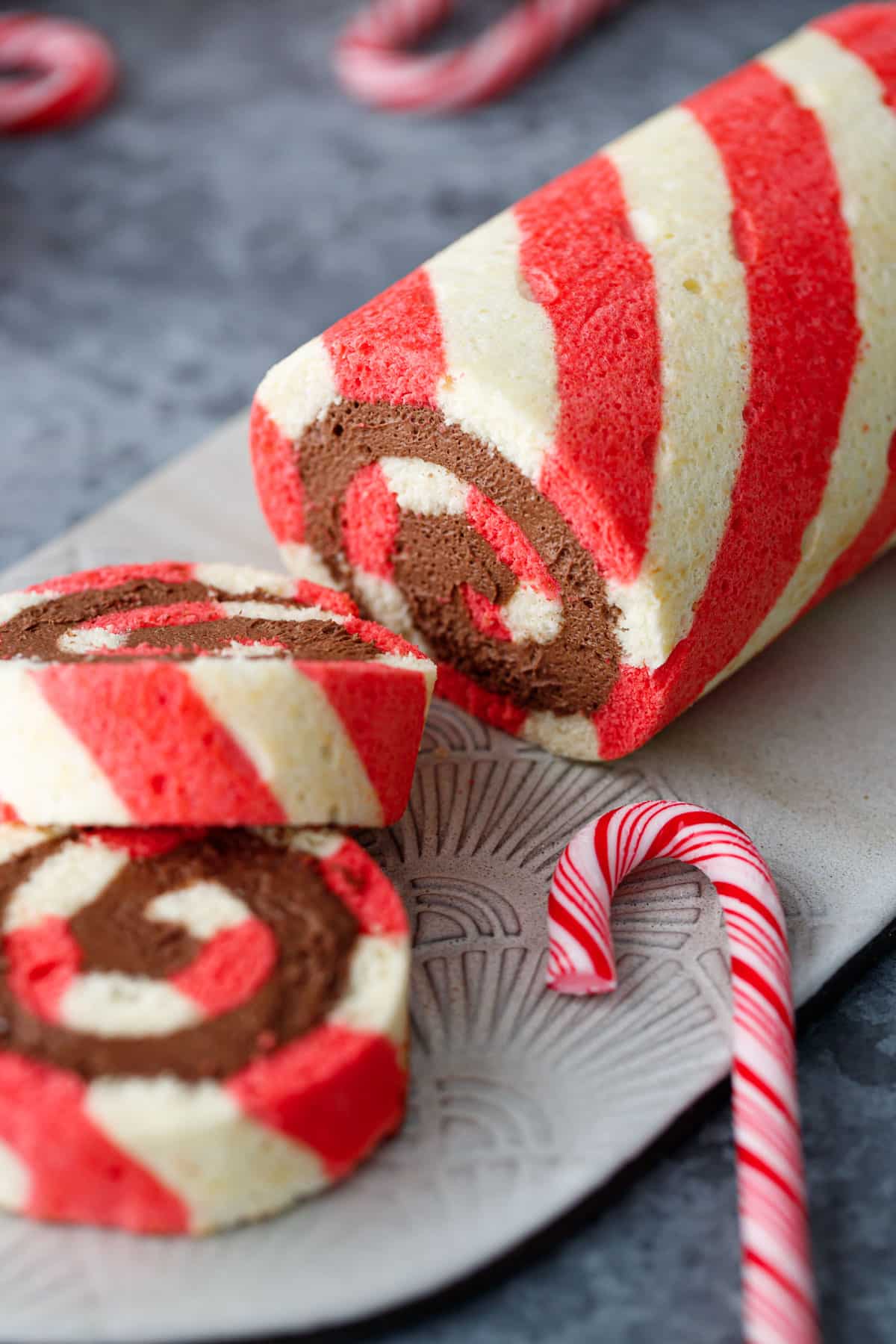Closeup view of a sliced red and white Peppermint cake roll, with a perfect spiral of chocolate peppermint whipped cream filling visible inside.