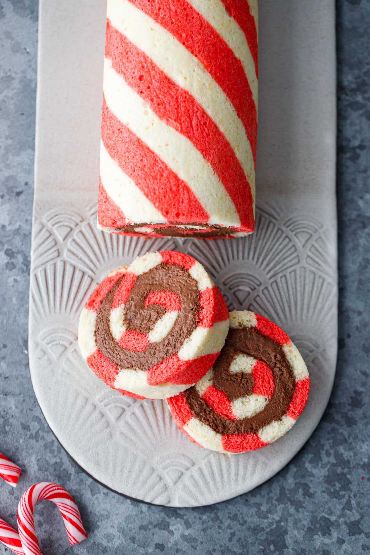 Overhead view of a red and white striped peppermint cake roll, two slices cut and laying on their sides to show the spiral of chocolate whipped cream filling inside.